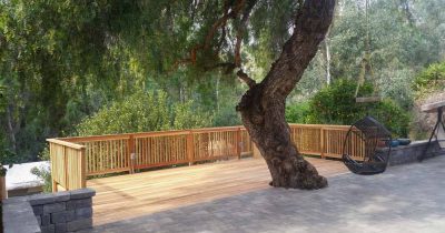 A Deck made of wood planks, attached to a concrete outdoor area with an undisturbed huge tree in the middle, and attached swing