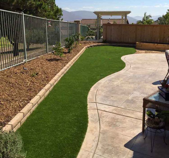 A concrete patio on a backyard with a portion of lawn and a raised garden near the fences