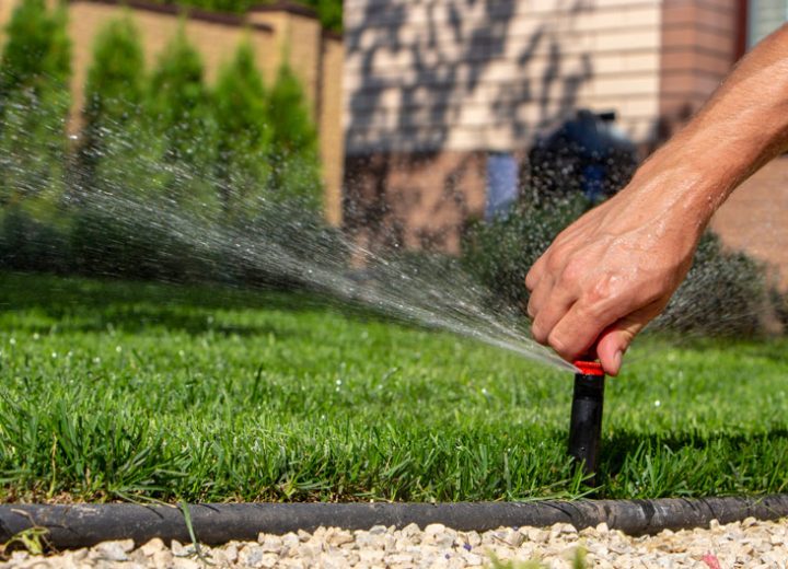 A hand manipulating the amount of water released from the sprinkler of a house yard